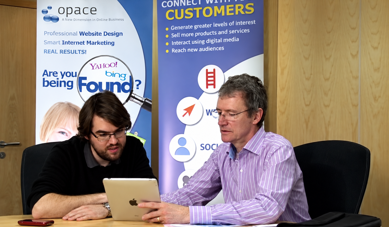 Opace team members working together with a tablet in front of Opace banners